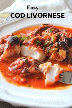 a white plate topped with fish covered in sauce and garnished with olives