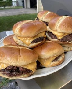 several hamburgers sitting on top of a white plate next to an open bbq