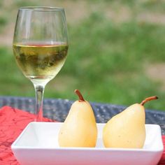 two pears on a plate next to a glass of white wine and a red tablecloth