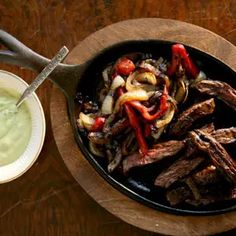 steak and vegetables in a skillet next to a bowl of ranch dressing on a wooden table