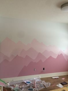 an empty room with pink and white mountains painted on the wall behind it, surrounded by construction materials