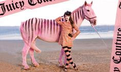 a woman standing next to a pink zebra on top of a sandy beach