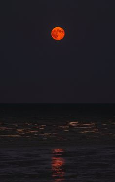 the full moon is seen over the ocean at night with bright orange lights on it