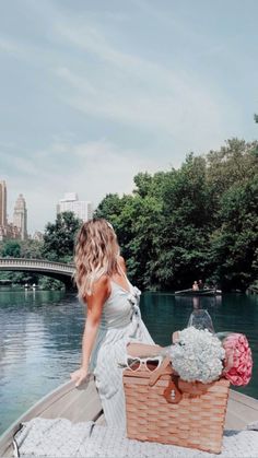 a woman is sitting in a boat on the water with flowers and a basket next to her