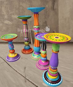 an assortment of colorfully painted candlesticks and stands on a wooden floor in front of a concrete wall