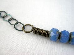 a blue beaded bracelet with two metal rings and some other beads on a white surface