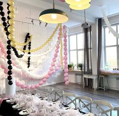 a room filled with tables and chairs covered in pink, white and black balloons hanging from the ceiling