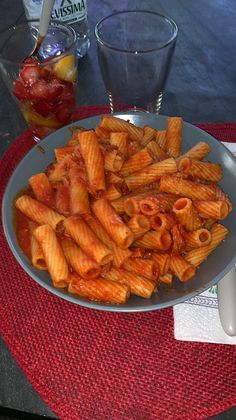 a plate full of pasta and sauce on a red place mat next to two glasses