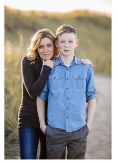 a woman standing next to a boy in front of some tall grass and sand dunes