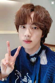 a young man making the peace sign with his hand while wearing a blue sweater and tie