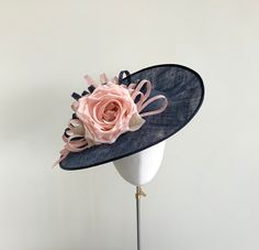 A classically elegant pale pink and navy blue fascinator, perfect for Royal Ascot, a wedding, or special occasion. Made in navy blue sinamay straw, this saucer shaped fascinator features a stunning pale blush pink silk dupion rose that sits to tho the front of the hat. Loops of sinamay straw in matching rose pink and navy twist around the rose and taper off to one side like ribbons.  Measuring 16 inches, this headpiece is fitted with a ribbon wrapped, double metal headband in a colour to blend i Navy Blue Fascinator, Royal Clothes, Blue Fascinator, Large Brim Hat, Pink Fascinator, Fancy Things, Ascot Hats, Metal Headband, Types Of Hats