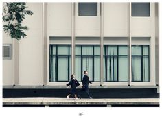 two people walking down the sidewalk in front of a building