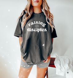 "♥ Looking for the perfect blend of comfort & style? Add one of our trendy Comfort color tees to your wardrobe! This design features a \"Raising Disciples\" graphic, perfect for the Christian mama wanting to display her faith! This design can also be purchased in a cozy sweatshirt option here! https://etsy.me/3SrbEpr ♥ About Printing/Garment: All of our apparel is printed using DTG printing in which the design is printed directly onto the garment which reduces cracking and peeling over time when cared for properly. Graphics are NOT vinyl. :) This shirt is a high-quality Comfort Color garment-dyed tee that comes in a variety of gorgeous hues for a lived-in vintage look. It is made of 100% cotton with a heavyweight feel for durability, but an unmatched softness for comfort! Comfort color gar Christian Tshirts Designs Woman, Christian Tees Women, Raising Disciples, Christian Tshirt, Faith Tees, Christian Tees, Comfort Colors Tee, Comfort Color, Dtg Printing