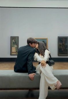 a man and woman sitting on a bench in an art museum, kissing each other