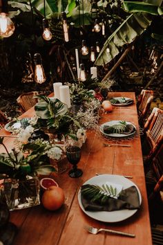 a wooden table topped with plates covered in flowers and greenery next to hanging lights