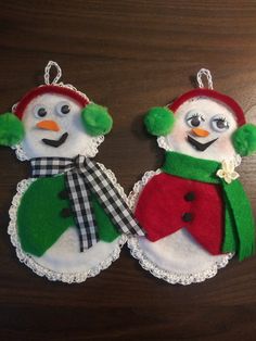 two felt snowmen with hats, scarfs and scarves hanging on a table