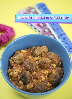 a blue bowl filled with meatballs and pasta on top of a yellow tablecloth