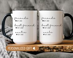 two personalized coffee mugs sitting on top of a wooden table next to a blanket