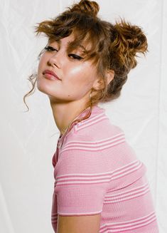 a young woman with her hair in a messy topknot looks off to the side