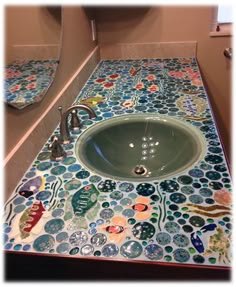 a bathroom sink that has been decorated with colorful tiles on the counter top and below it is a mirror