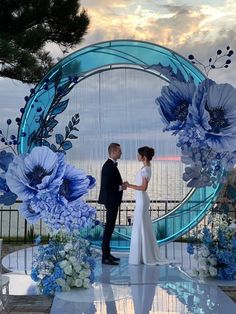 a bride and groom standing in front of an artistic backdrop with blue flowers on it