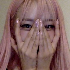 a woman with pink hair covering her face and hands over her eyes, looking at the camera