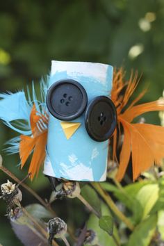 a blue and orange owl sitting on top of a tree branch with two buttons in it's eyes