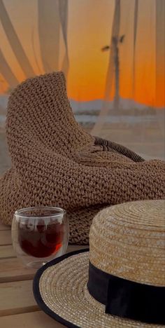 a straw hat sitting on top of a wooden table next to a glass of wine