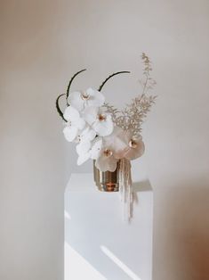 a white vase with flowers in it sitting on a table next to a light colored wall