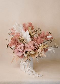 a white vase filled with lots of pink and white flowers on top of a table