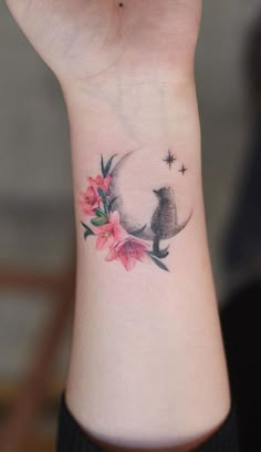 a woman's wrist tattoo with a cat sitting on the moon and flowers around it