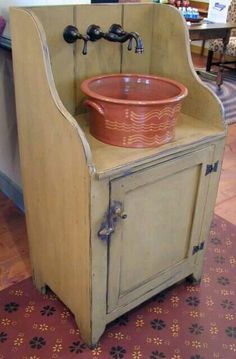 an old fashioned sink with a red bowl on it's cabinet and faucet