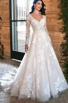 a woman standing in front of a wooden wall wearing a wedding dress with long sleeves