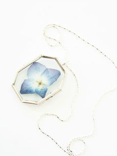 a necklace with a blue flower in the center on a white background and a silver chain