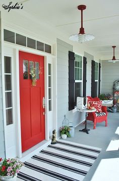 the front porch is decorated with red and black doors, striped rugs, and potted plants