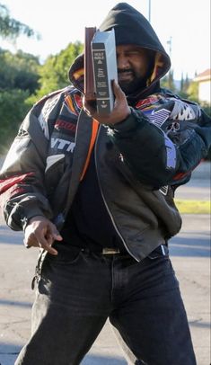 a man in a black jacket is holding up a book and pointing it at the camera