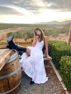 a woman in a white dress sitting on top of a barrel next to a wooden barrel