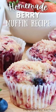 three blueberry muffins sitting on top of a wooden cutting board next to a bowl of fruit