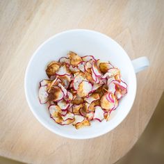 a white bowl filled with radishes on top of a wooden table next to a spoon