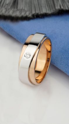 two tone gold and silver wedding band with diamond in the center, on top of a blue cloth