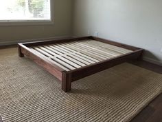 a wooden bed frame sitting on top of a carpeted floor next to a window