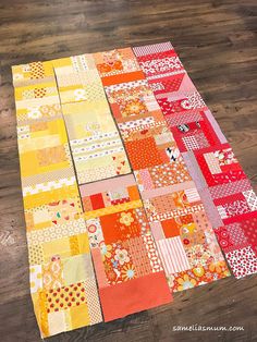 an orange and yellow patchwork quilt laying on top of a wooden floor