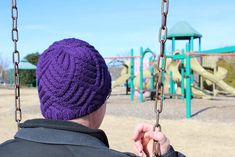 a person in a purple hat on a swing at a playground with swings and slides