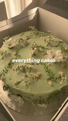 a green cake with white flowers and greenery on top sits in a cardboard box