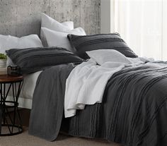 a bed with grey and white comforters in a bedroom next to a table on the floor