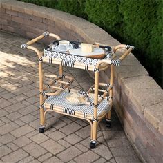 a serving cart with plates and bowls on it sitting in front of a brick wall