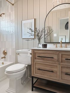 a white toilet sitting next to a bath tub in a bathroom under a mirror above a sink