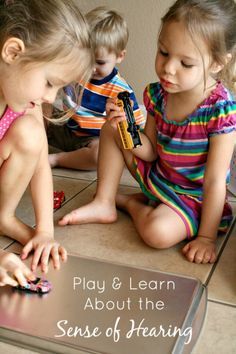 three young children playing with toys on the floor in front of a sign that says play and learn about the sense of hear