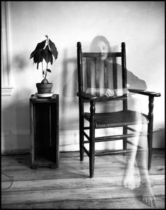 a black and white photo of a person sitting in a chair next to a potted plant