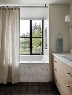 a bathroom with a large window and marble counter top next to a sink under a shower curtain